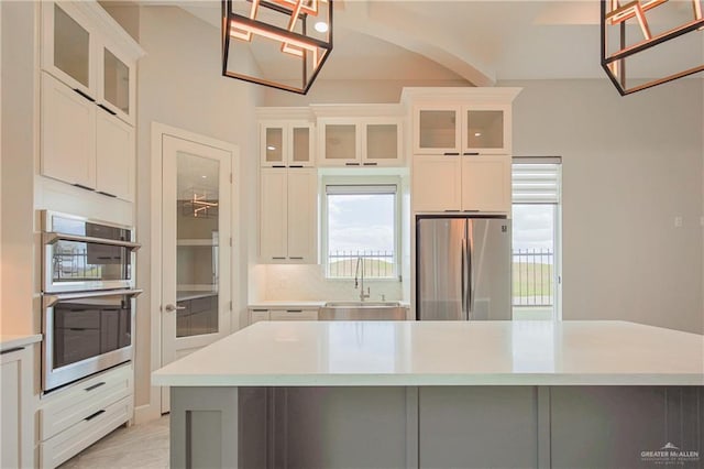 kitchen with light countertops, appliances with stainless steel finishes, glass insert cabinets, white cabinetry, and a sink