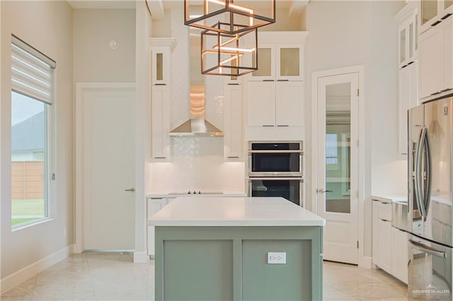 kitchen with light countertops, backsplash, appliances with stainless steel finishes, white cabinets, and wall chimney exhaust hood