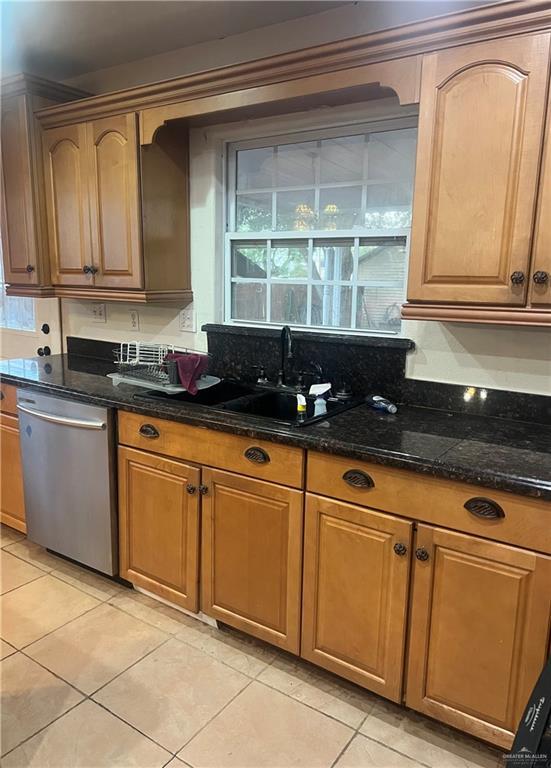 kitchen with light tile patterned floors, stainless steel dishwasher, dark stone counters, and sink