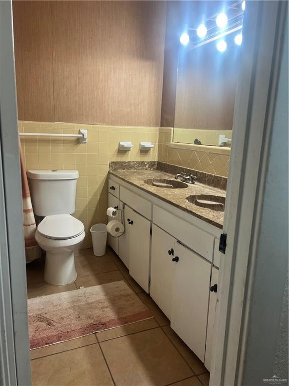 bathroom with tile patterned flooring, vanity, toilet, and tile walls