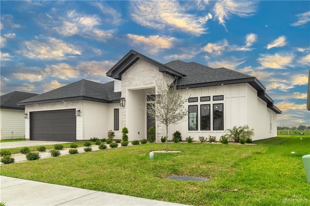 prairie-style home featuring board and batten siding, driveway, stone siding, a front yard, and a garage