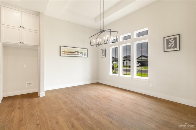 unfurnished dining area featuring a chandelier, light wood-style flooring, baseboards, and a tray ceiling