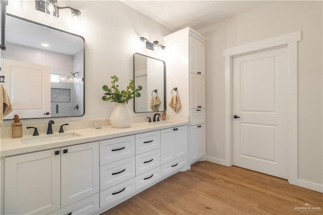 bathroom with double vanity, a shower, wood finished floors, and a sink