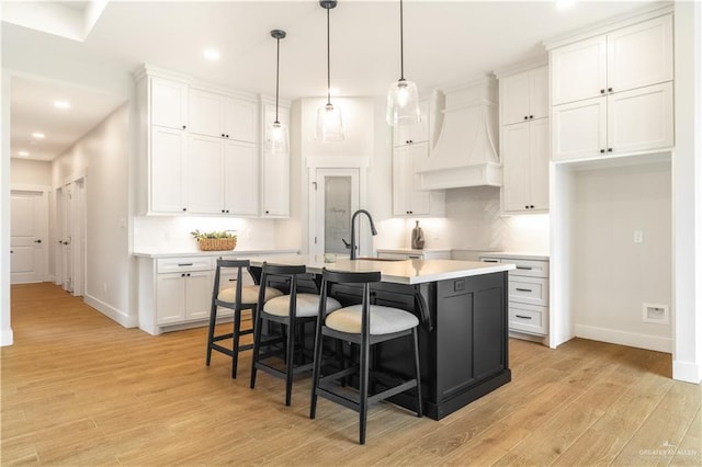 kitchen with white cabinets, baseboards, custom exhaust hood, and a kitchen island with sink