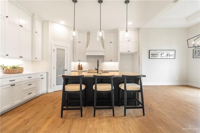 kitchen with white cabinets, custom exhaust hood, a sink, and light wood-type flooring