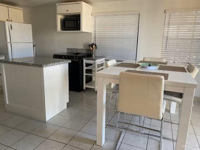 kitchen featuring black appliances, a kitchen bar, stone counters, and light tile patterned flooring