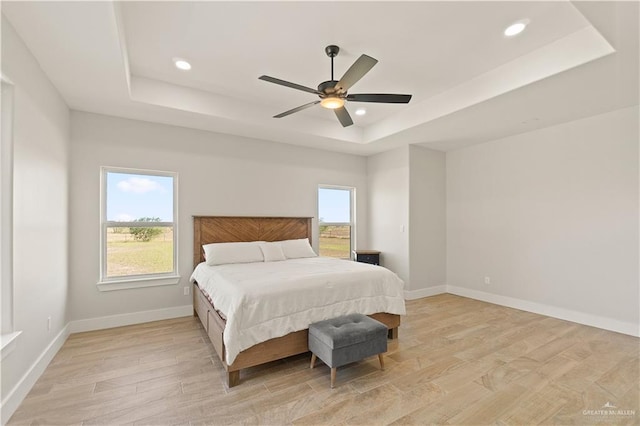 bedroom featuring ceiling fan, light hardwood / wood-style flooring, a tray ceiling, and multiple windows