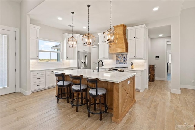 kitchen with white cabinets, premium range hood, an island with sink, and appliances with stainless steel finishes