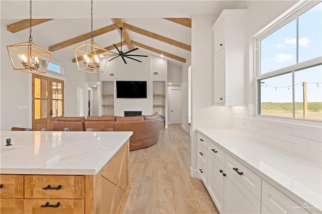 kitchen with light stone countertops, beam ceiling, decorative light fixtures, light hardwood / wood-style flooring, and white cabinetry