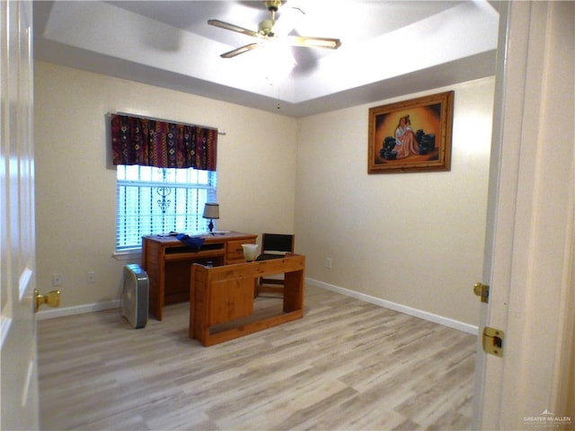 office with a ceiling fan, baseboards, a raised ceiling, and light wood-style floors