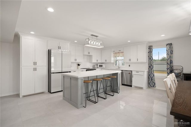 kitchen with white cabinets, dishwasher, a kitchen island, fridge, and a breakfast bar area