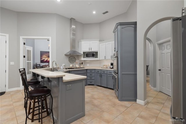 2513 Kings Dr, Edinburg, TX 78539 - kitchen featuring stainless steel appliances, gray cabinets, a peninsula, wall chimney range hood, and a breakfast bar area