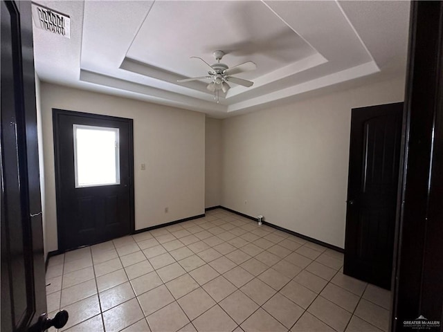 interior space with a raised ceiling, ceiling fan, and light tile patterned flooring