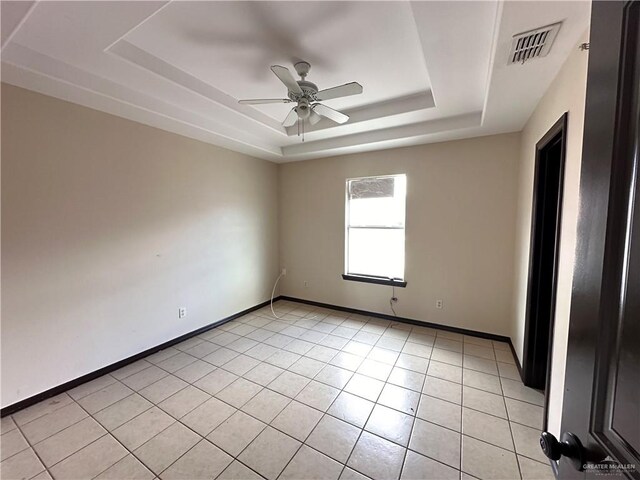 tiled empty room featuring ceiling fan and a tray ceiling