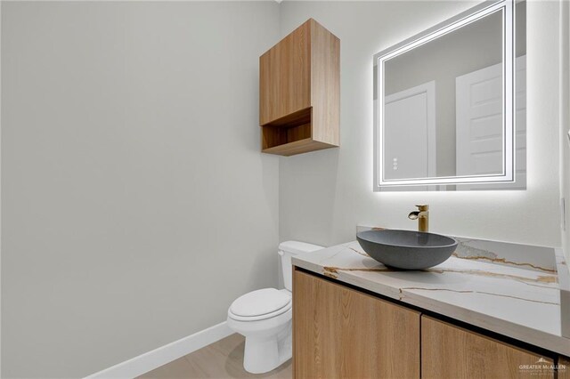 half bathroom featuring toilet, vanity, and baseboards