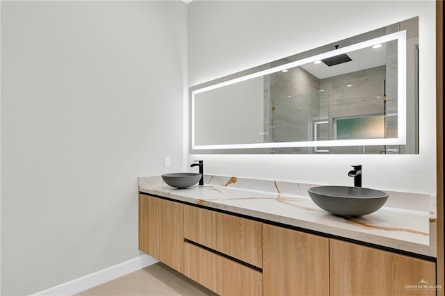 full bathroom with double vanity, baseboards, a sink, and a marble finish shower