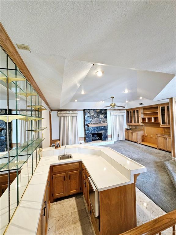 kitchen with sink, a textured ceiling, kitchen peninsula, light colored carpet, and a fireplace