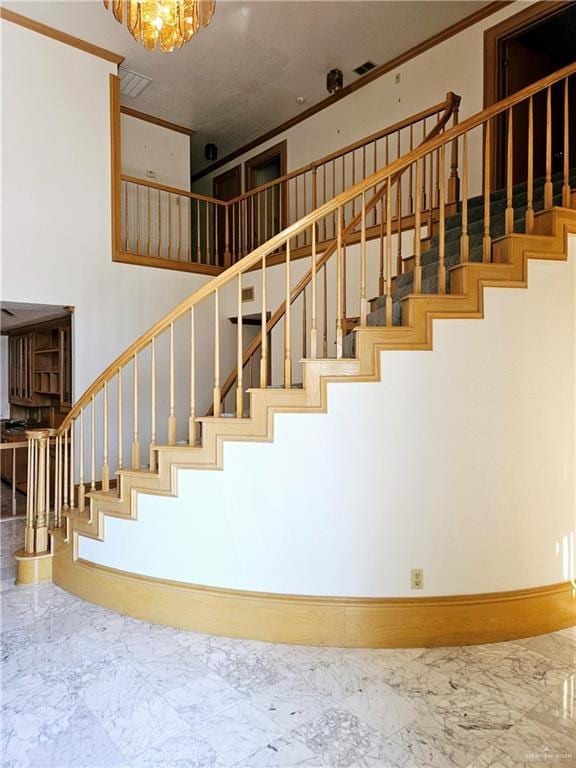 staircase with a high ceiling, crown molding, and an inviting chandelier