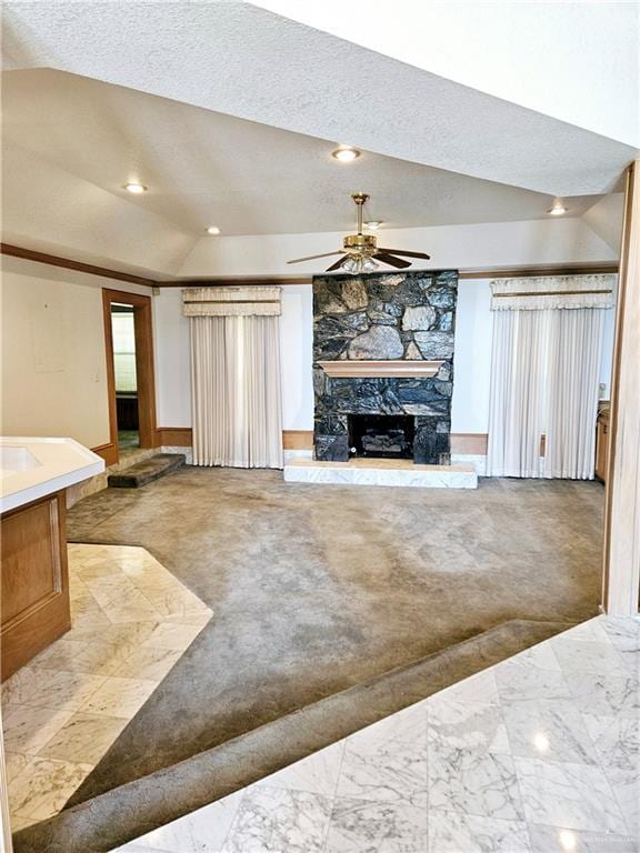 living room with ceiling fan, lofted ceiling, a stone fireplace, and light colored carpet