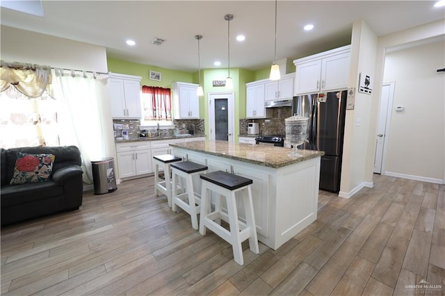 29082 Reynolds Dr, La Feria, TX 78559 - kitchen featuring freestanding refrigerator, a kitchen island, under cabinet range hood, light wood-type flooring, and recessed lighting