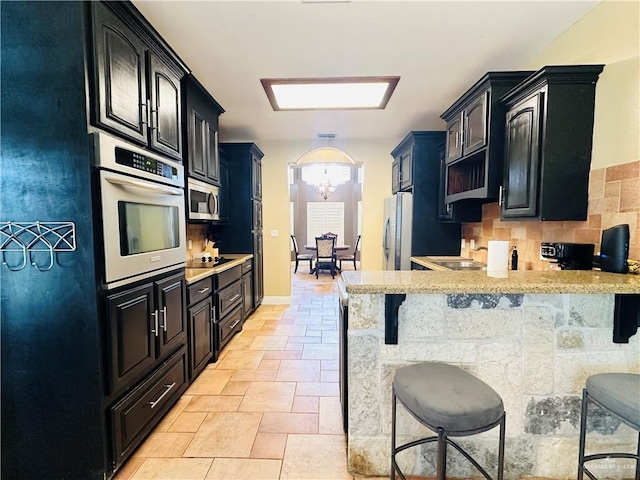 kitchen featuring stainless steel appliances, a notable chandelier, backsplash, kitchen peninsula, and a breakfast bar area