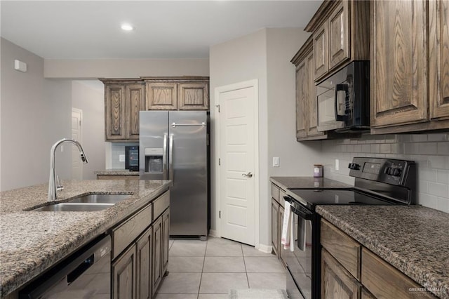 kitchen featuring sink, backsplash, stone countertops, light tile patterned floors, and black appliances