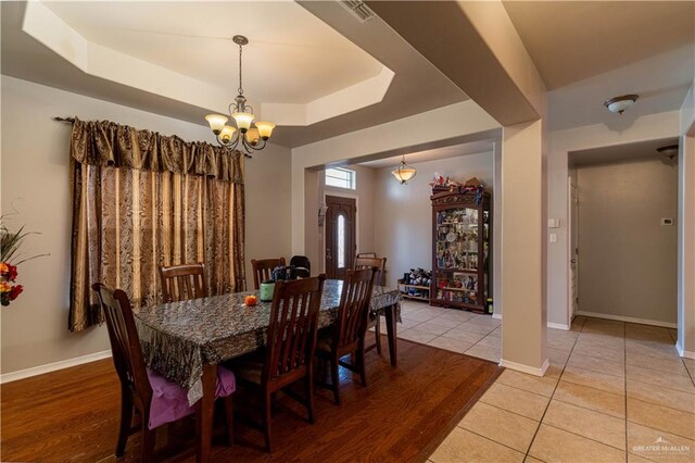 dining room featuring a raised ceiling, light wood-type flooring, and a chandelier