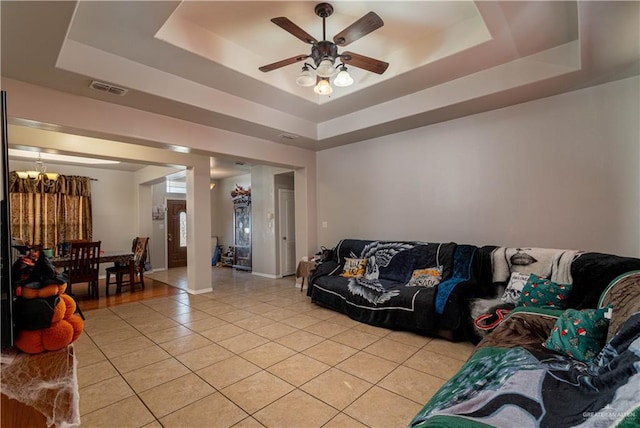 tiled living room with ceiling fan with notable chandelier and a tray ceiling