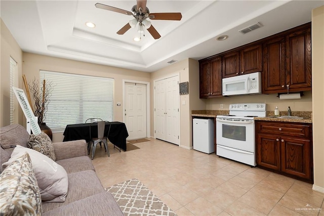 kitchen with ceiling fan, light stone countertops, a raised ceiling, white appliances, and dark brown cabinets