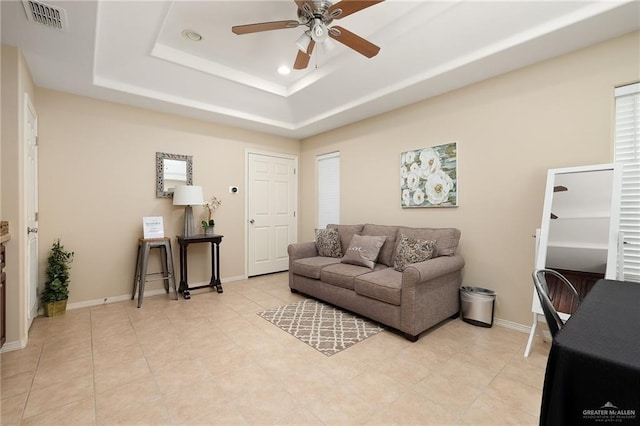 living room with a raised ceiling, ceiling fan, and light tile patterned floors