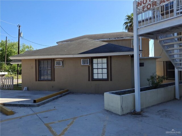 view of side of property featuring a patio area, roof with shingles, and stucco siding