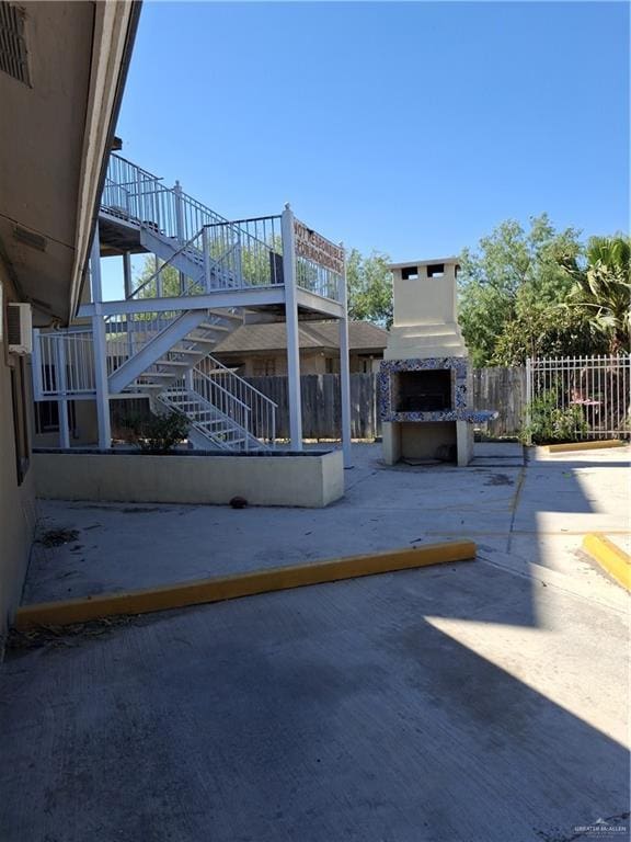 view of patio featuring fence, an outdoor fireplace, and stairs