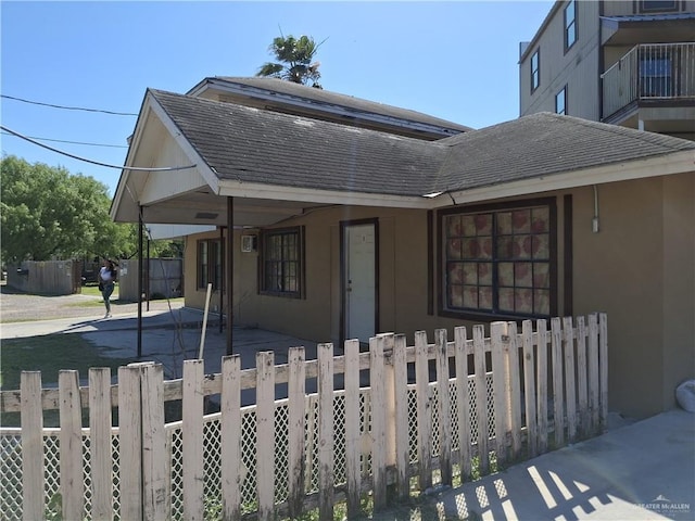 bungalow-style home with a carport, a fenced front yard, stucco siding, and roof with shingles