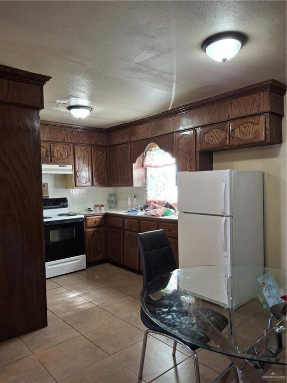 kitchen with light countertops, a textured ceiling, freestanding refrigerator, under cabinet range hood, and range with electric stovetop