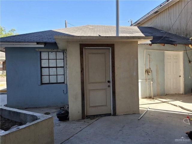 entrance to property featuring a patio area, stucco siding, and roof with shingles