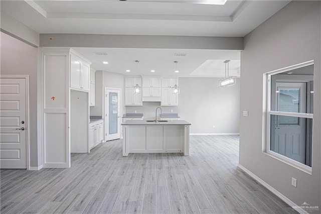 kitchen featuring a sink, white cabinets, light wood-type flooring, a center island with sink, and pendant lighting