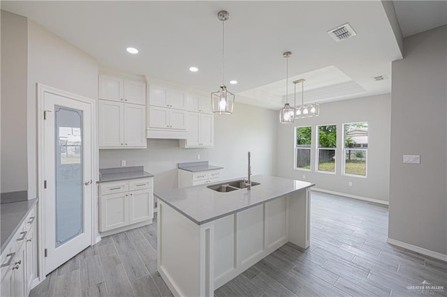 kitchen featuring pendant lighting, a kitchen island with sink, a raised ceiling, and white cabinetry