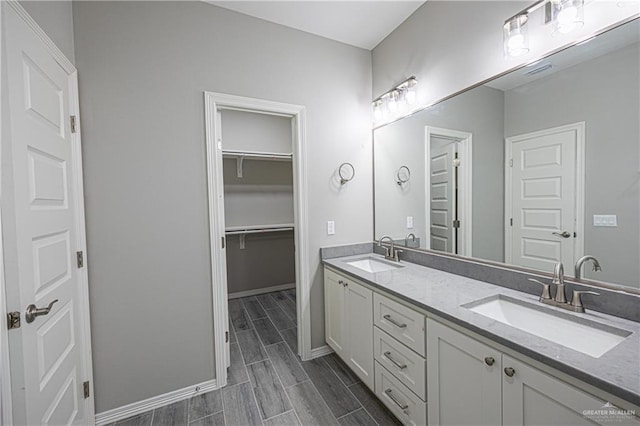 full bath with double vanity, wood finish floors, a sink, and baseboards