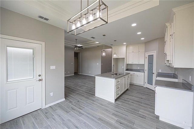 kitchen featuring a kitchen island with sink, visible vents, white cabinets, open floor plan, and dark countertops