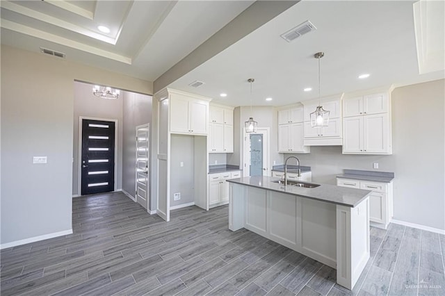 kitchen featuring a center island with sink, visible vents, white cabinets, hanging light fixtures, and a sink