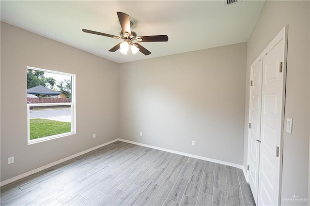 spare room featuring light wood finished floors, a ceiling fan, and baseboards