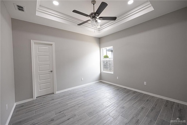 empty room with a tray ceiling, visible vents, baseboards, and wood finished floors