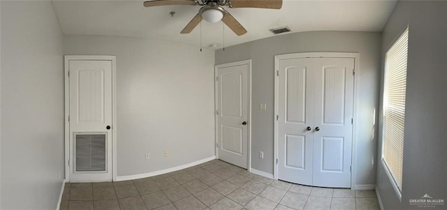 unfurnished bedroom featuring ceiling fan, light tile patterned floors, and multiple closets