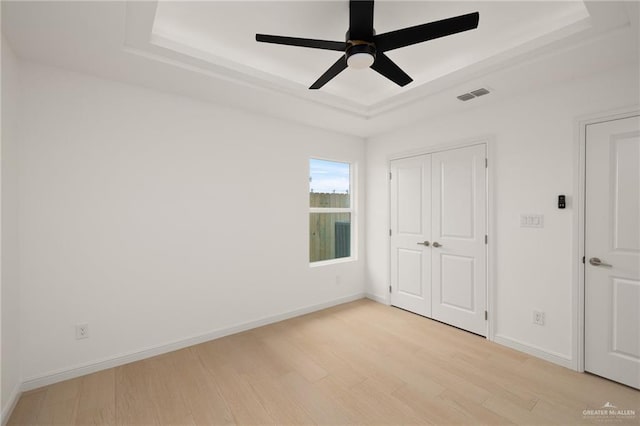 unfurnished bedroom with visible vents, a closet, baseboards, a raised ceiling, and light wood-style flooring