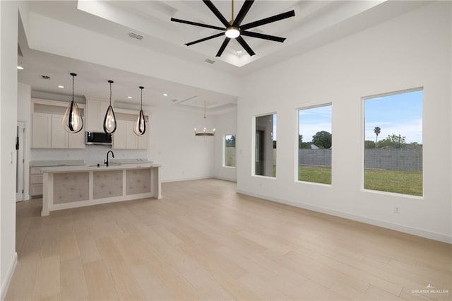 unfurnished living room featuring visible vents, recessed lighting, a tray ceiling, light wood finished floors, and ceiling fan with notable chandelier