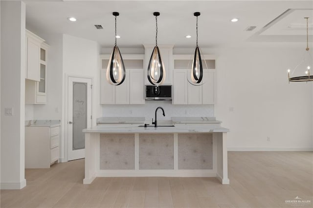 kitchen featuring an inviting chandelier, a sink, light countertops, stainless steel microwave, and a center island with sink