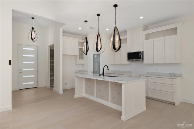 kitchen featuring white cabinets, a sink, an island with sink, light wood-style flooring, and stainless steel microwave