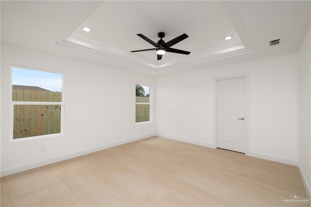 spare room with visible vents, light wood-style flooring, ceiling fan, and a tray ceiling