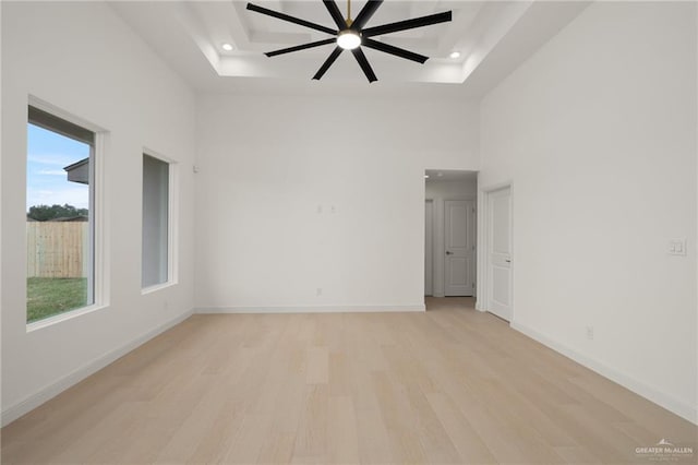 spare room with a raised ceiling, recessed lighting, a high ceiling, and light wood finished floors