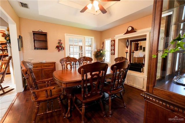 dining area with a raised ceiling, ceiling fan, and dark wood-type flooring